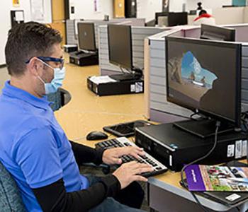 Student sitting at desk working on laptop in computer lab setting