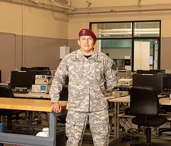 Veteran in military fatigues with red beret standing in a room of workstations